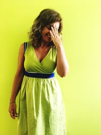 Young woman standing against yellow background