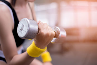 Midsection of woman lifting dumbbell