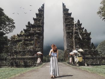 Woman standing on road leading towards gate