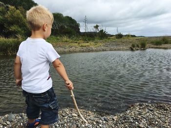Boy standing on riverbank against sky