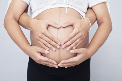 Midsection of woman touching heart shape against white background