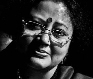 Close-up portrait of mature woman wearing eyeglasses and bindi in dark