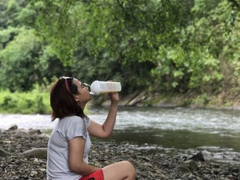 Side view of young woman drinking by river