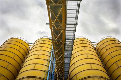 Low angle view of yellow silos at industry against sky