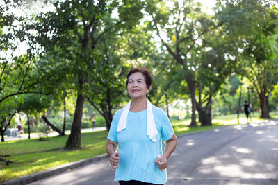 Thoughtful senior woman running on road against trees at park