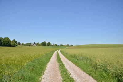 Dirt road amidst field against clear sky