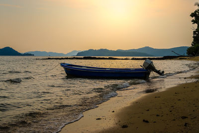 Boat moored on beach against sky during sunset