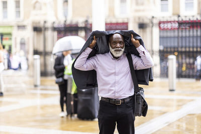 Senior businessman covering head with suit on footpath