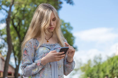 Young woman using mobile phone against sky