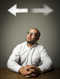 Portrait of man with eyeglasses on table against wall