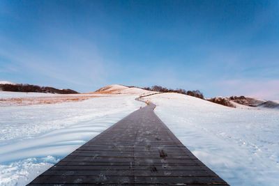 Boardwalk by snowy landscape against blue sky