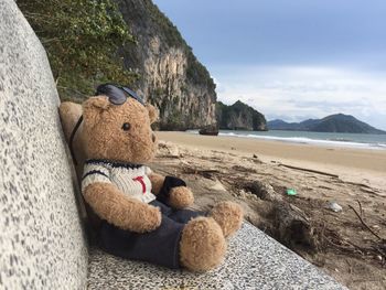 Teddy bear on seat at beach against sky