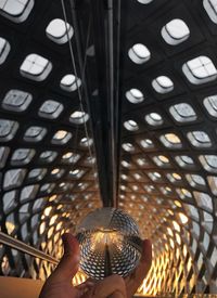 Cropped hand of person holding crystal ball against patterned ceiling