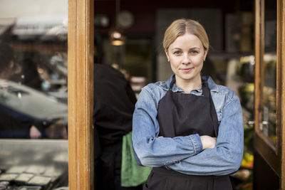 Portrait of confident saleswoman standing arms crossed at supermarket entrance