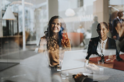 Smiling businesswoman with female colleague seen through glass