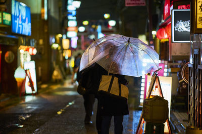 Rear view of people with umbrellas on street at night