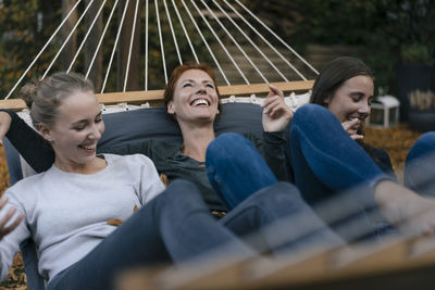 Carefree mother with two teenage girls lying in hammock in garden in autumn