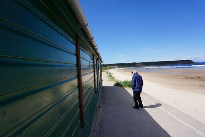 Rear view of man walking on beach against clear sky