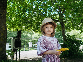 Portrait of small girl wearing lilac dress and summer hat and horse