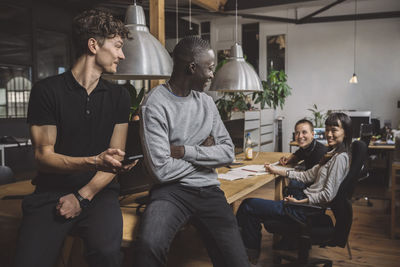 Smiling businessmen talking to female colleagues at workplace