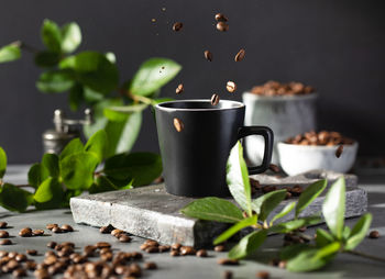 Roasted coffee beans surrounded by green leaves are flying into a black mug. the theme of cafes,