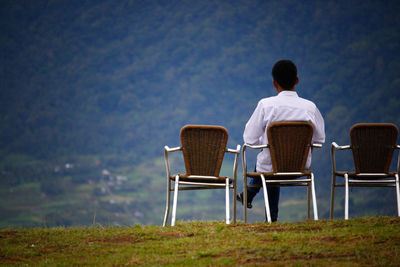 Rear view of man sitting on chair at mountain