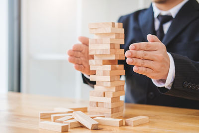 Midsection of businessman protecting stacked wooden blocks on table