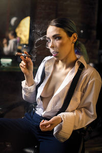 Portrait of seductive woman smoking cigar at home