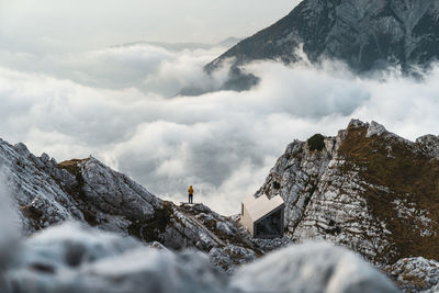 Distant view of man standing by cliff against cloudscape