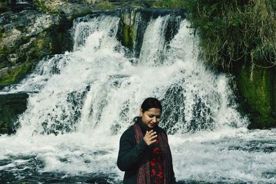 Full length of young woman standing against waterfall
