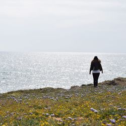 Rear view of man walking on sea shore against sky
