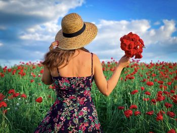Low section of woman by red poppy flowers on field against sky