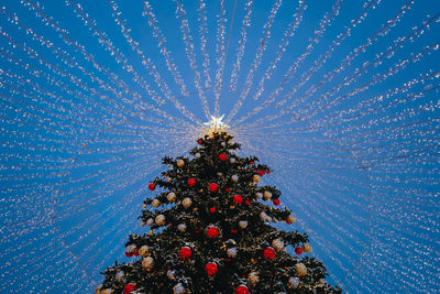 Christmas tree with red toy balls, star and golden lights in the festive evening city bokeh garlands