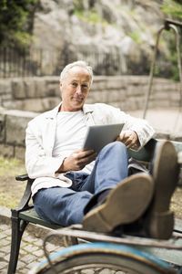 Portrait of businessman with feet up on bicycle holding digital tablet at park