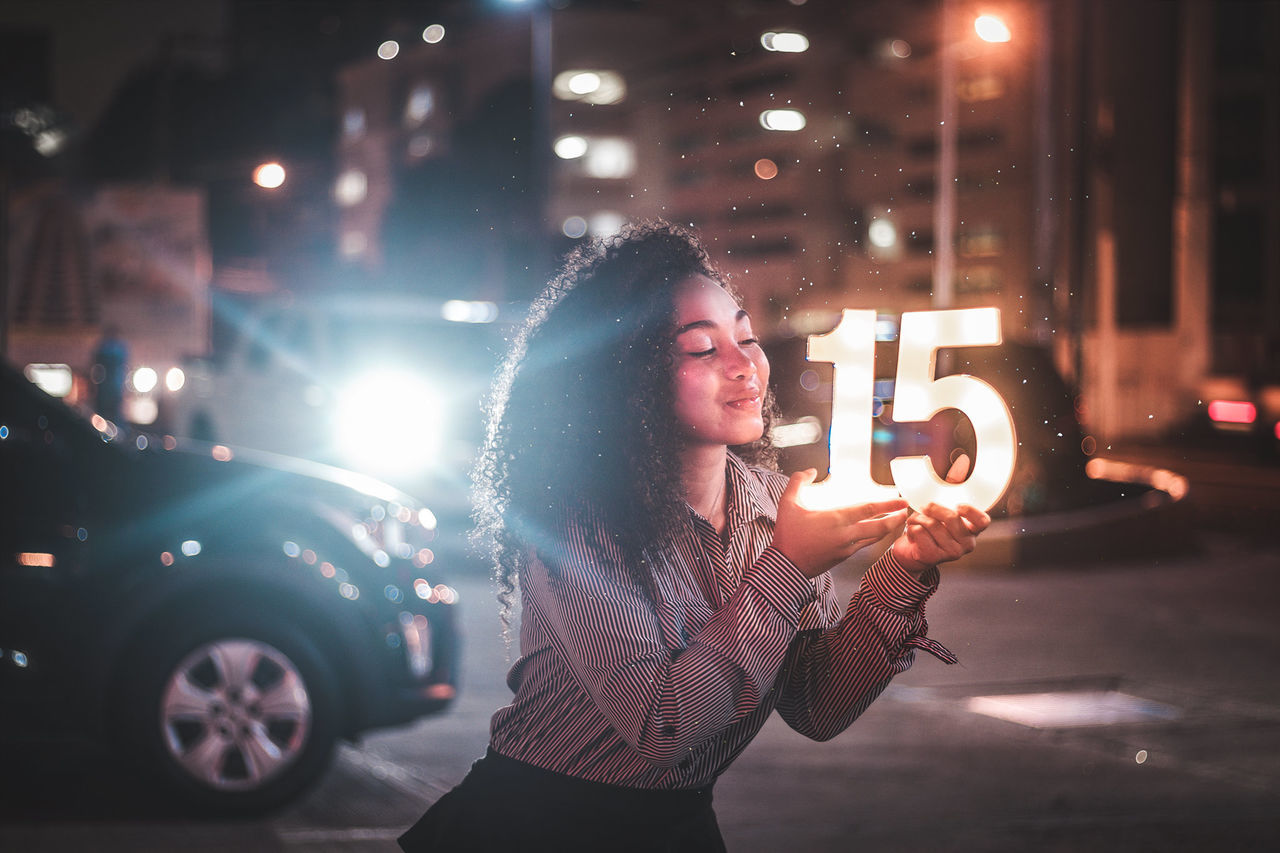 one person, illuminated, night, city, lifestyles, young adult, street, car, motor vehicle, transportation, real people, architecture, young women, leisure activity, glowing, mode of transportation, standing, looking, hairstyle, hair, city street, beautiful woman, outdoors