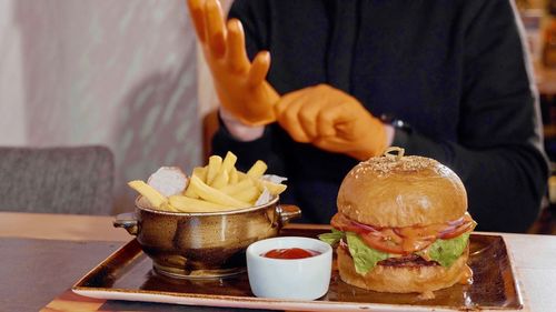 Midsection of man wearing glove with burger served on table