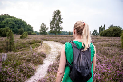 Rear view of woman with backpack while walking on field against sky