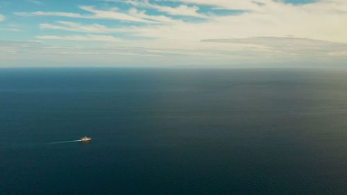 Small passenger ferry cruising in the open blue sea against blue sky with clouds, aerial view. 