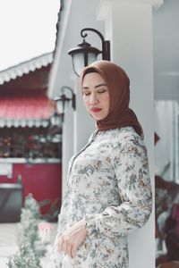 Woman looking at camera while standing against built structure