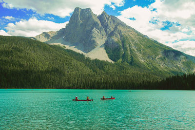 People rowing boat against grassy mountain in emerald lake at yoho national park