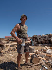 Full length of man holding axe while standing against clear blue sky