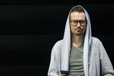 Portrait of man wearing hooded shirt while holding mobile phone