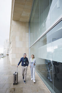 Smiling businessman and businesswoman walking by glass wall