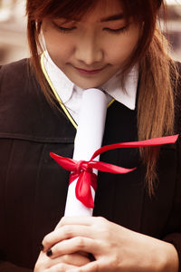 Close-up of young woman in graduation gown holding degree