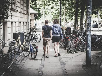 Full length rear view of men walking on sidewalk by building in city