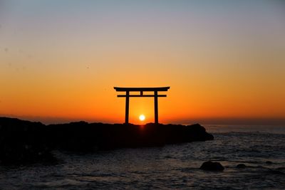 Silhouette rock in sea against orange sky