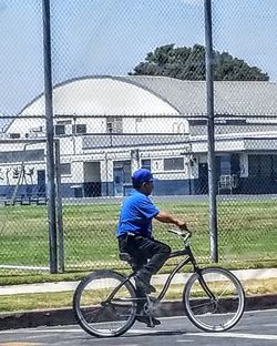 Rear view of man riding bicycle on chainlink fence