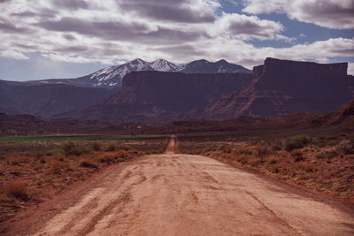 Dirt road leading towards mountains against sky