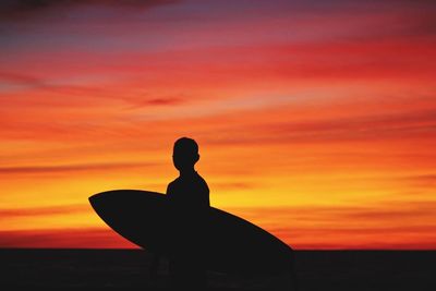 Silhouette man carrying surfboard against scenic sky