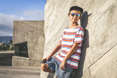 Young woman wearing sunglasses standing against built structure